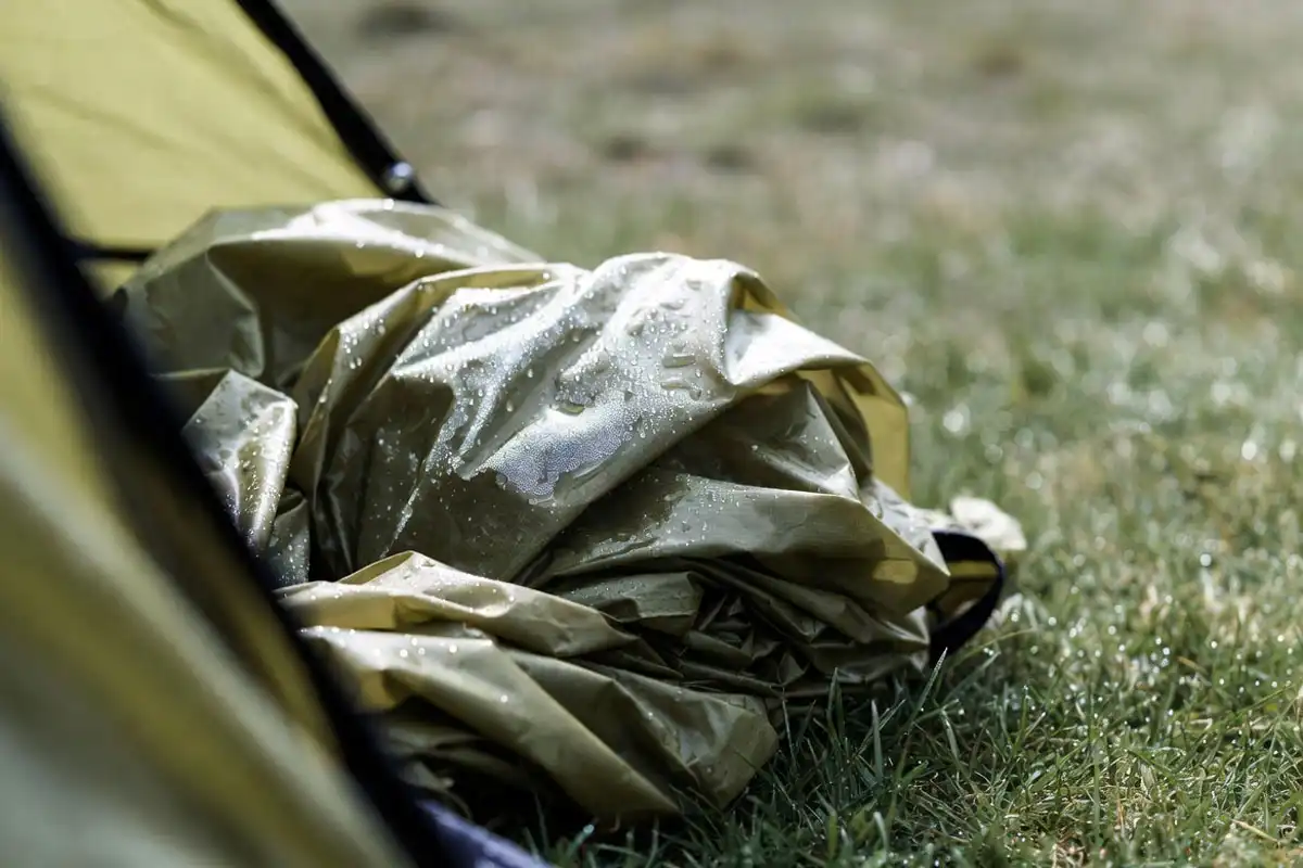 Damp camping tent stuffed into a wet nylon stuff sack with visible moisture