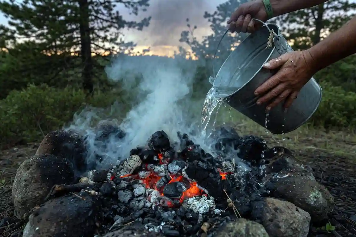 Camper pouring water on campfire to fully extinguish coals