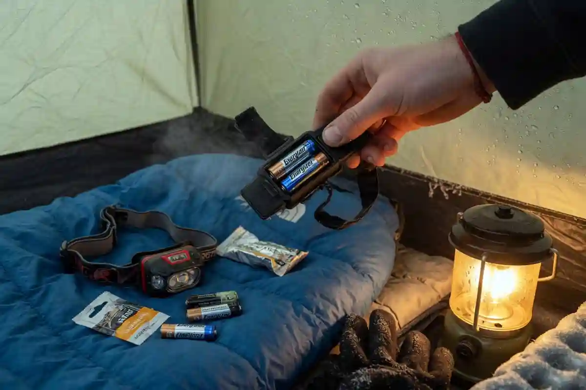 Camper changing batteries in a headlamp inside a tent
