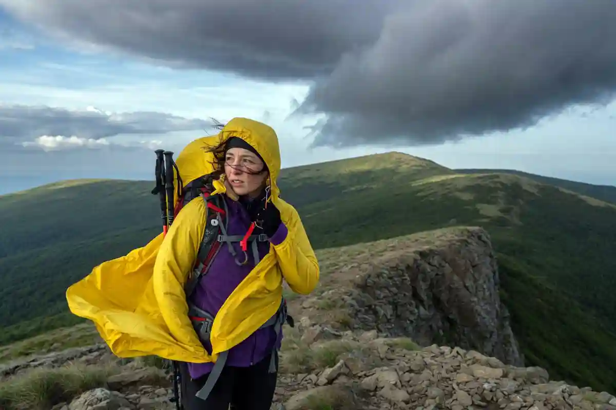 Hiker putting on a rain jacket as clouds gather over a ridge