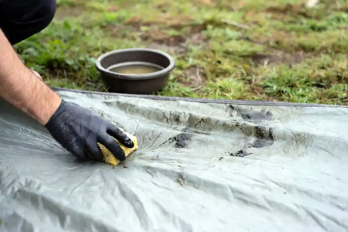 Camper scrubbing dark mold from a tent rainfly with a sponge