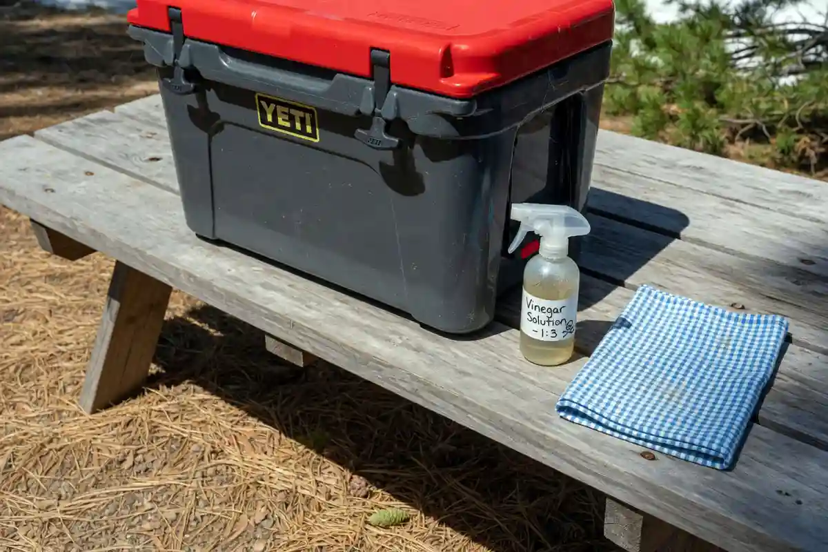 Hard-sided cooler with tight latches on a camping table with vinegar spray bottle nearby