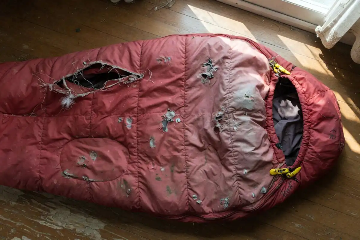 Worn red sleeping bag with fabric tear and broken zipper