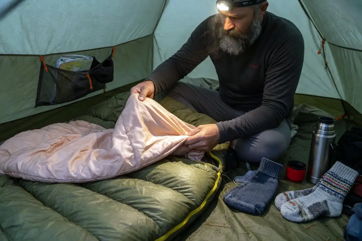 Camper adding a liner to a sleeping bag inside a tent
