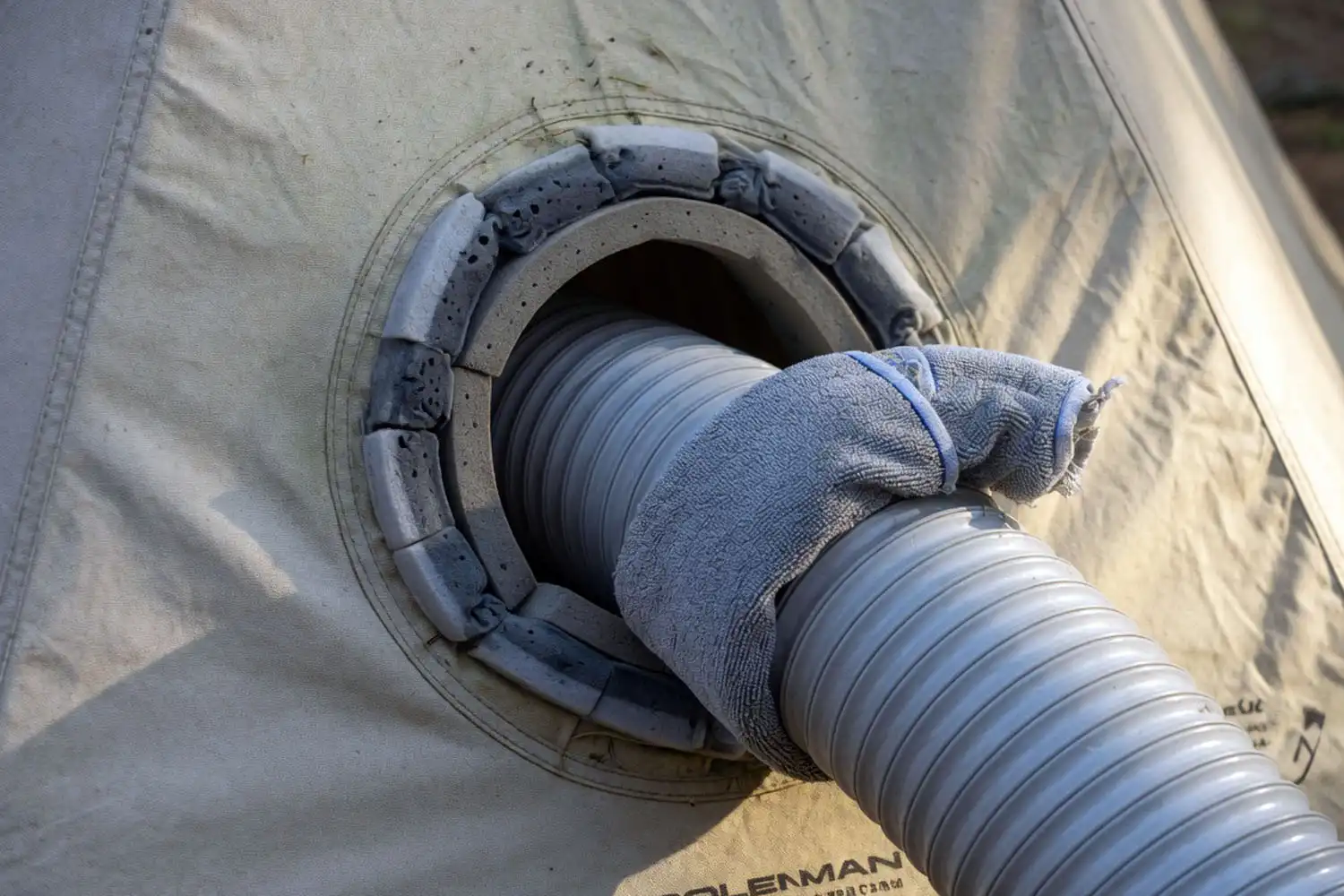a silver AC exhaust hose sealed into a tent's AC port with foam insulation around the gap