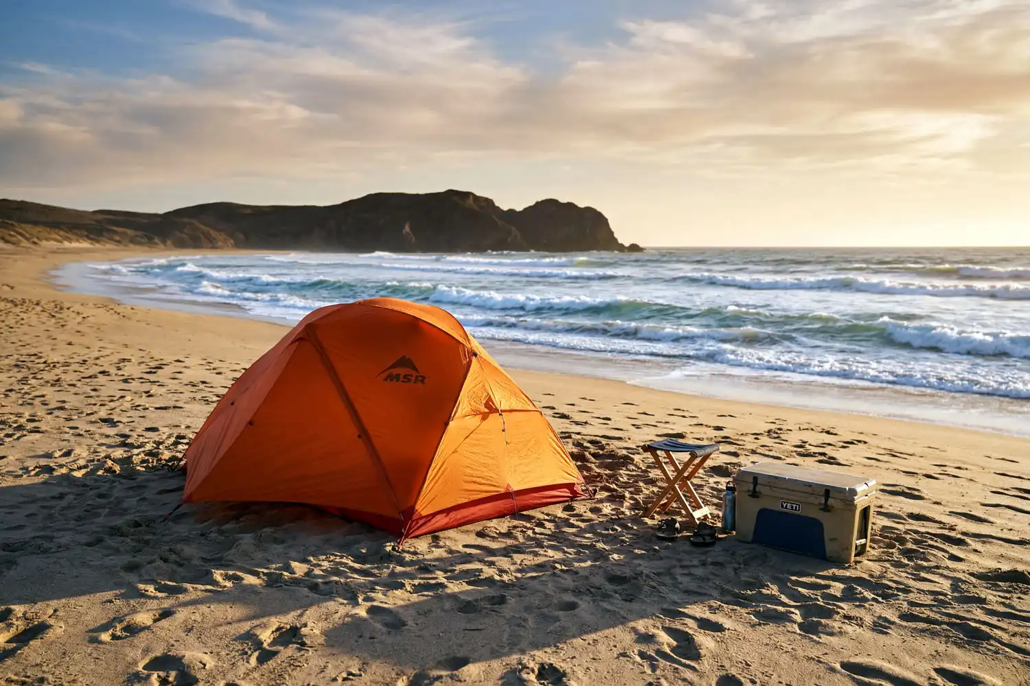 Orange dome tent set up on a sandy beach above the high tide line during golden hour sunset over the ocean
