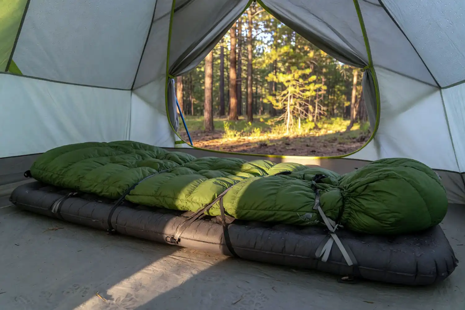 Down camping quilt secured with straps to a sleeping pad inside a backpacking tent with vestibule open