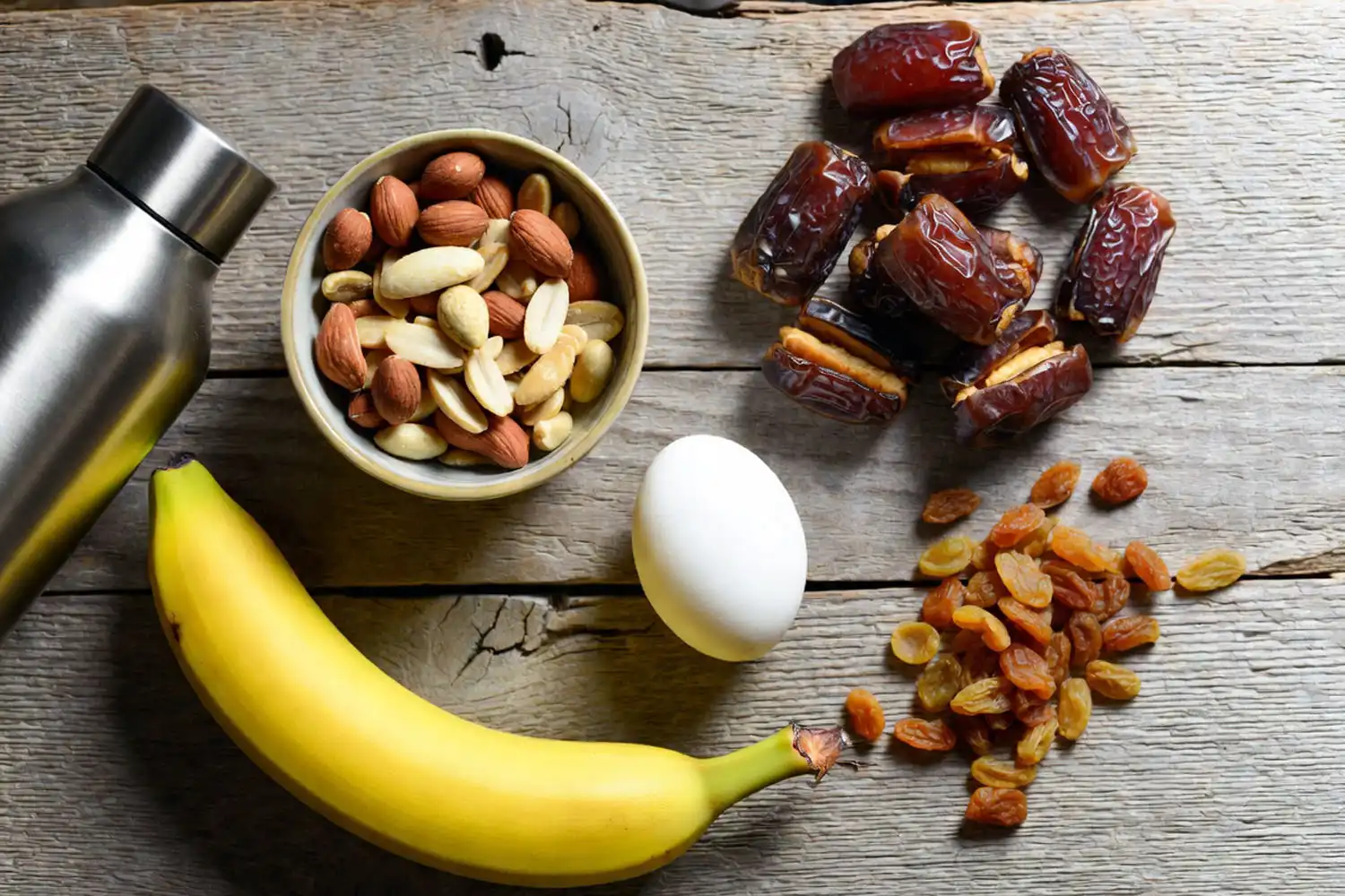 healthy hiking snacks including nuts, dates, raisins, banana, and water bottle on a wooden table