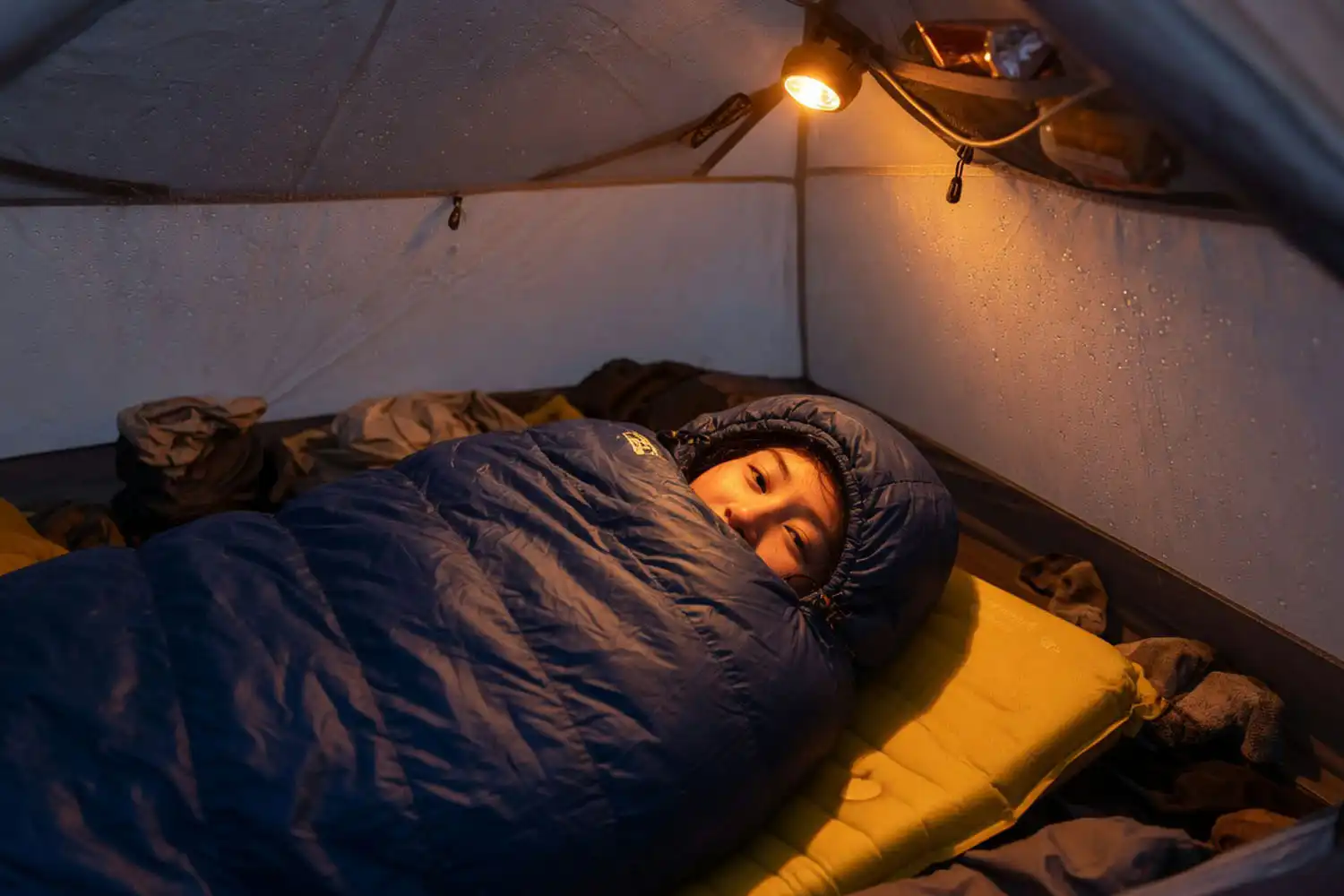 Camper resting inside a zipped mummy sleeping bag with the hood cinched tight inside a backpacking tent
