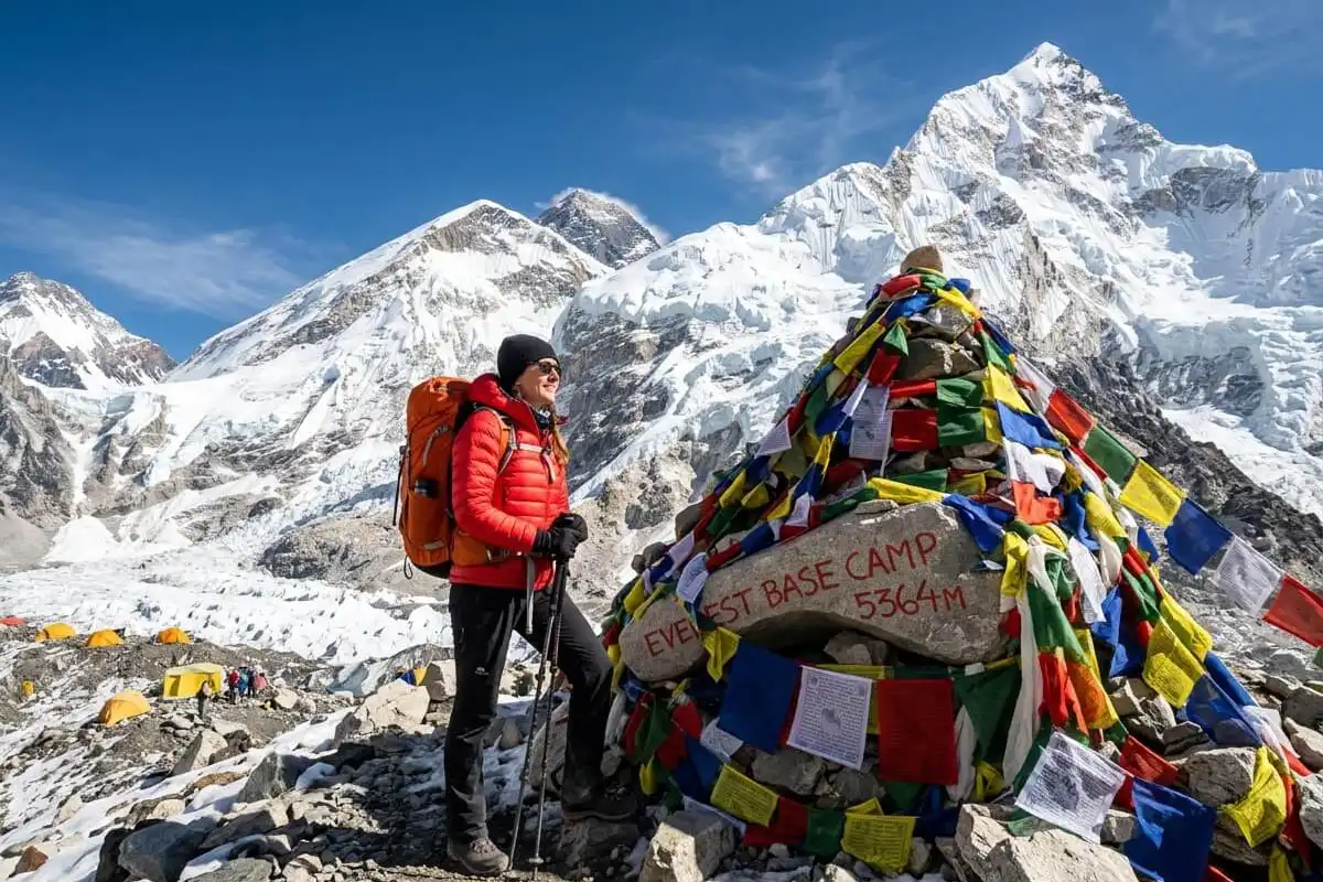 Trekker standing near the Everest Base Camp marker stone with prayer flags and the Khumbu Icefall in the background