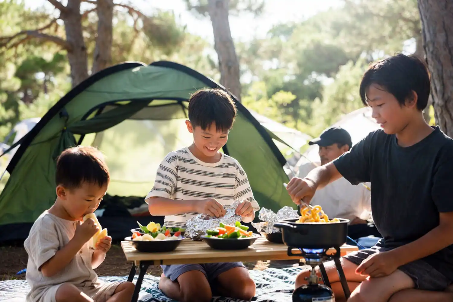A toddler eating banana slices while an older child wraps a foil packet and a tween stirs a pot at a family campsite