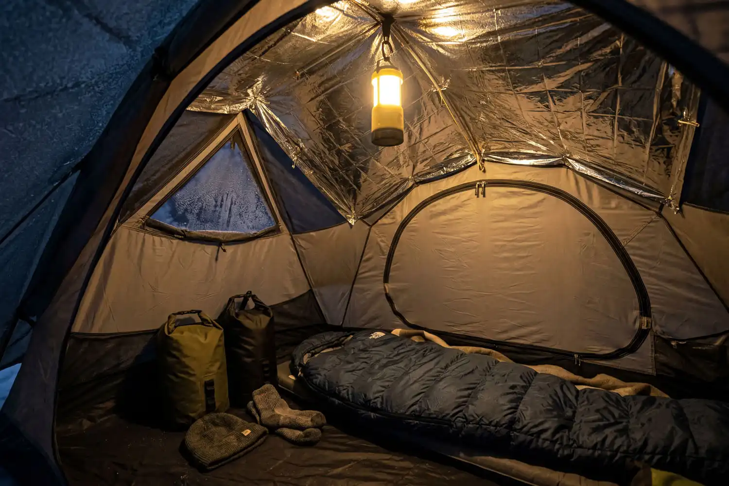 Silver mylar emergency blanket pinned to the inner ceiling of a winter tent at night with lantern light reflecting down