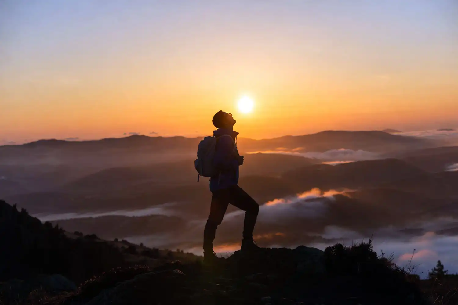 Solo hiker standing on a mountain ridge at sunrise with arms relaxed and breathing deeply