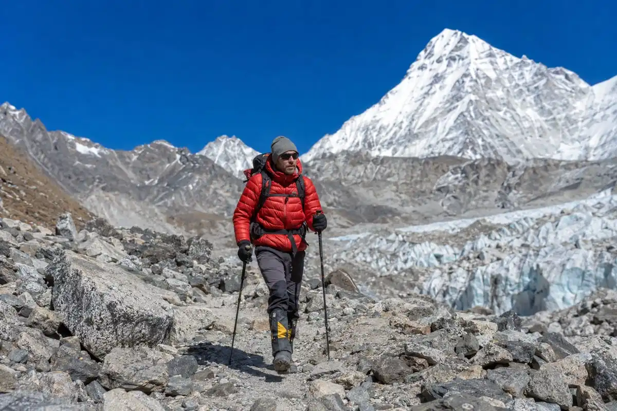 Solo trekker with backpack and trekking poles walking on rocky Khumbu Glacier moraine approaching Everest Base Camp