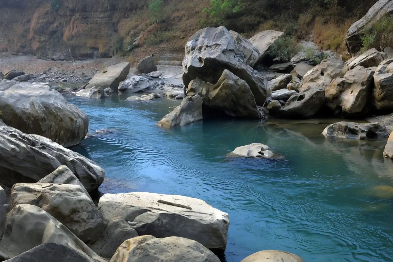 Huge grey boulders filling the Sangu River at the Boro Pathor area upstream of Tindu with a small boat passing between them