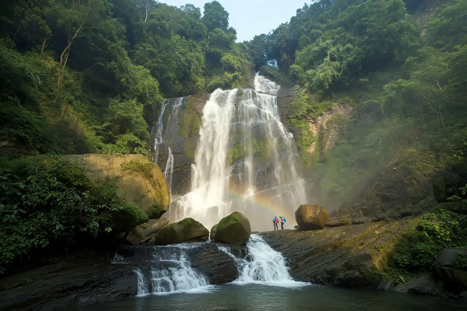 The wide terraced Jadipai Waterfall flowing over black rock with green hills in Bandarban, Bangladesh