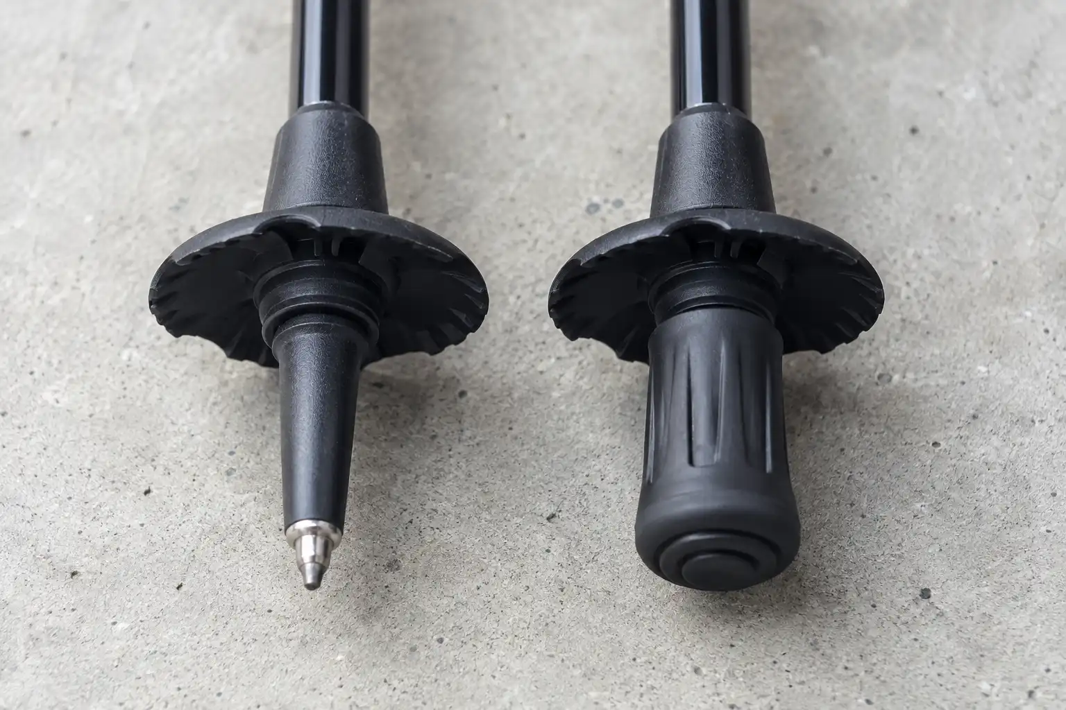 Close-up comparison of a sharp carbide trekking pole tip next to the same pole fitted with a blunt rubber tip protector