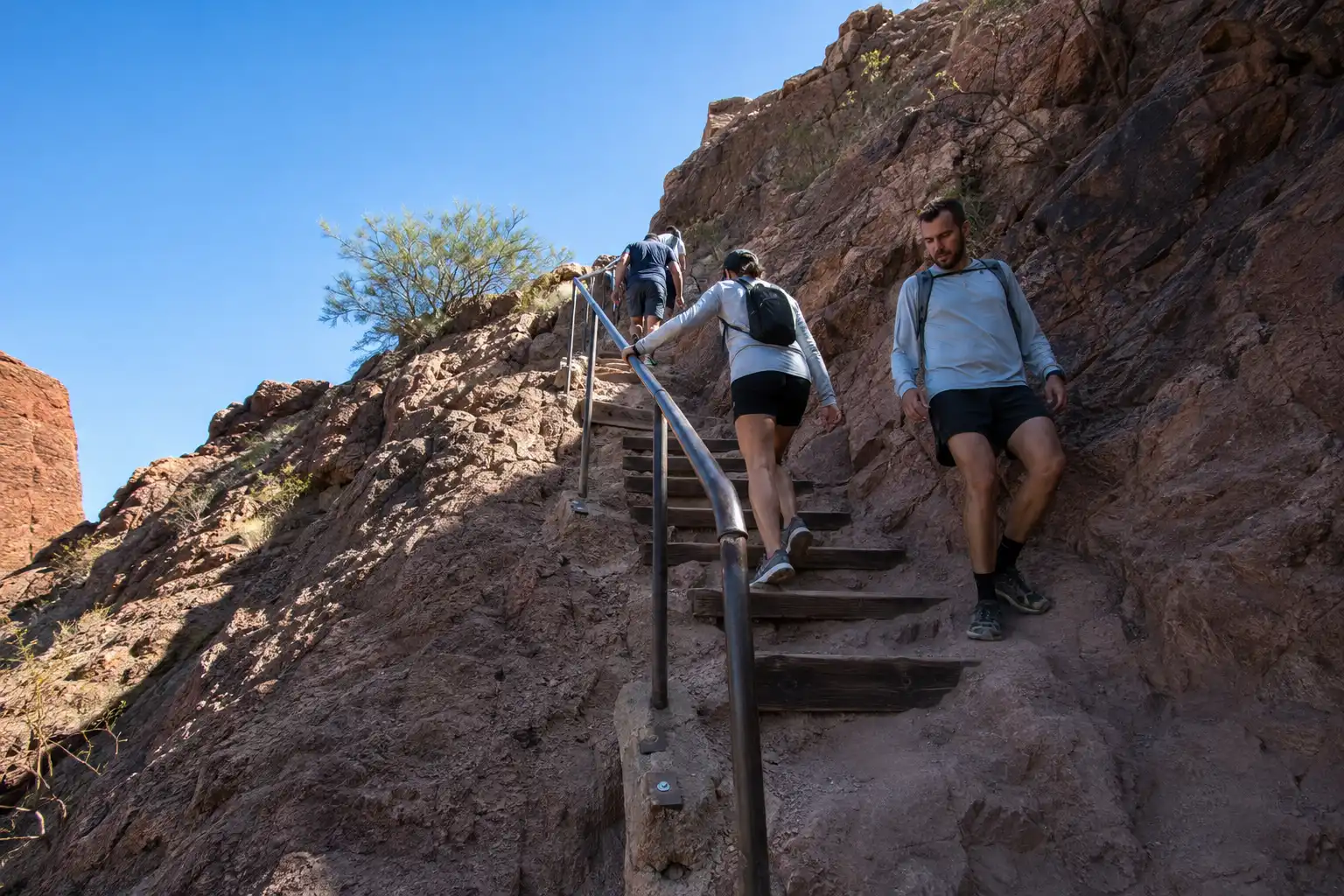 Hikers using steel handrails and railroad tie steps on the steep Echo Canyon Trail section of Camelback Mountain