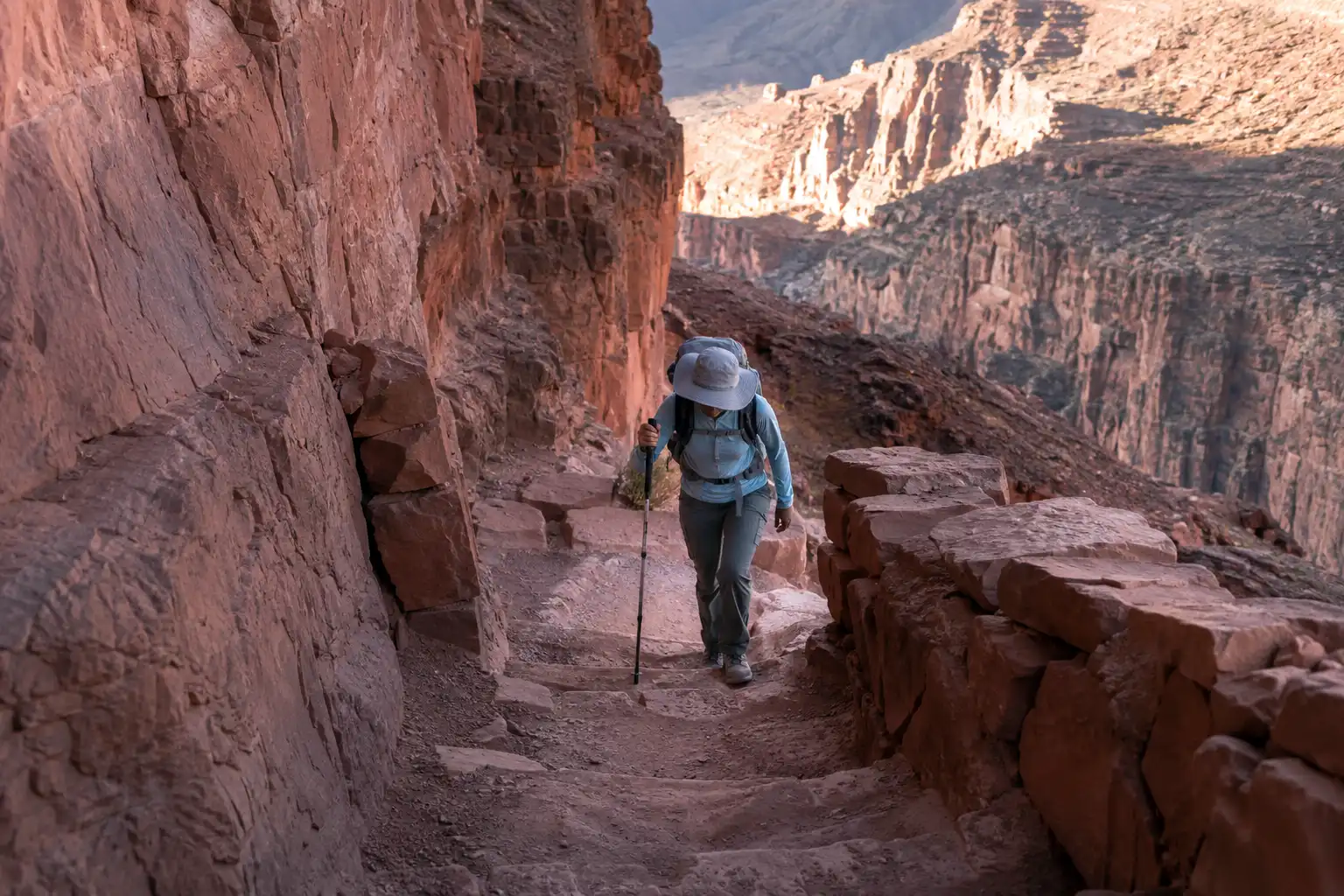 Hiker in a sun hat climbing a steep switchback section of the Bright Angel Trail during the uphill return to the South Rim