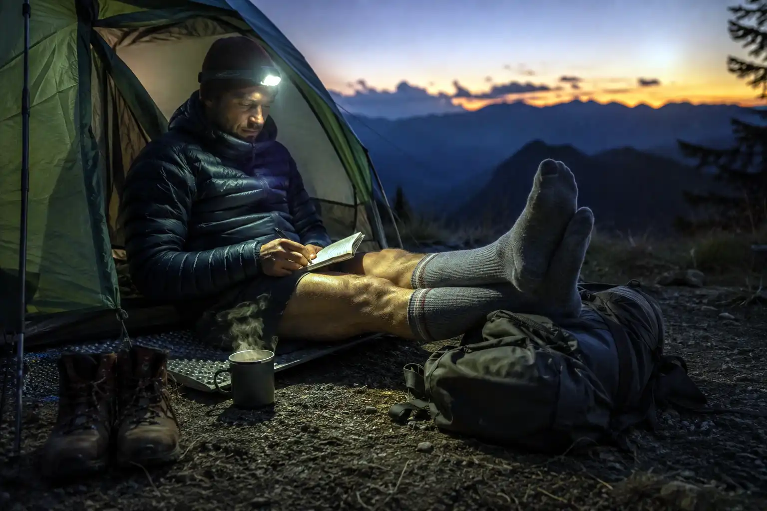 Hiker sitting outside a tent in the evening with legs propped on a pack, wearing compression socks after a long day of hiking