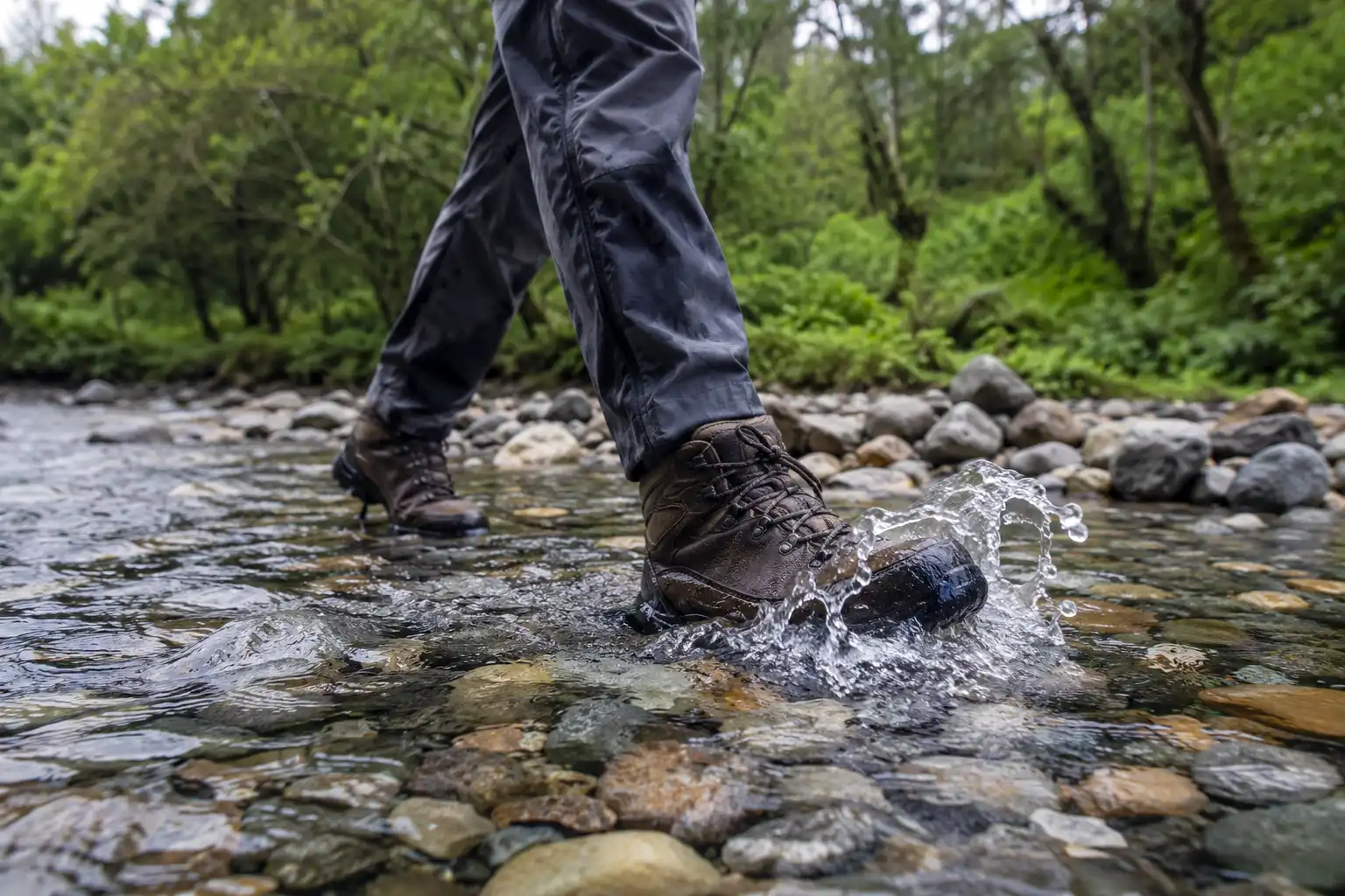 Hiker crossing a shallow rocky stream in mid-cut waterproof hiking boots with water rising near the boot collar