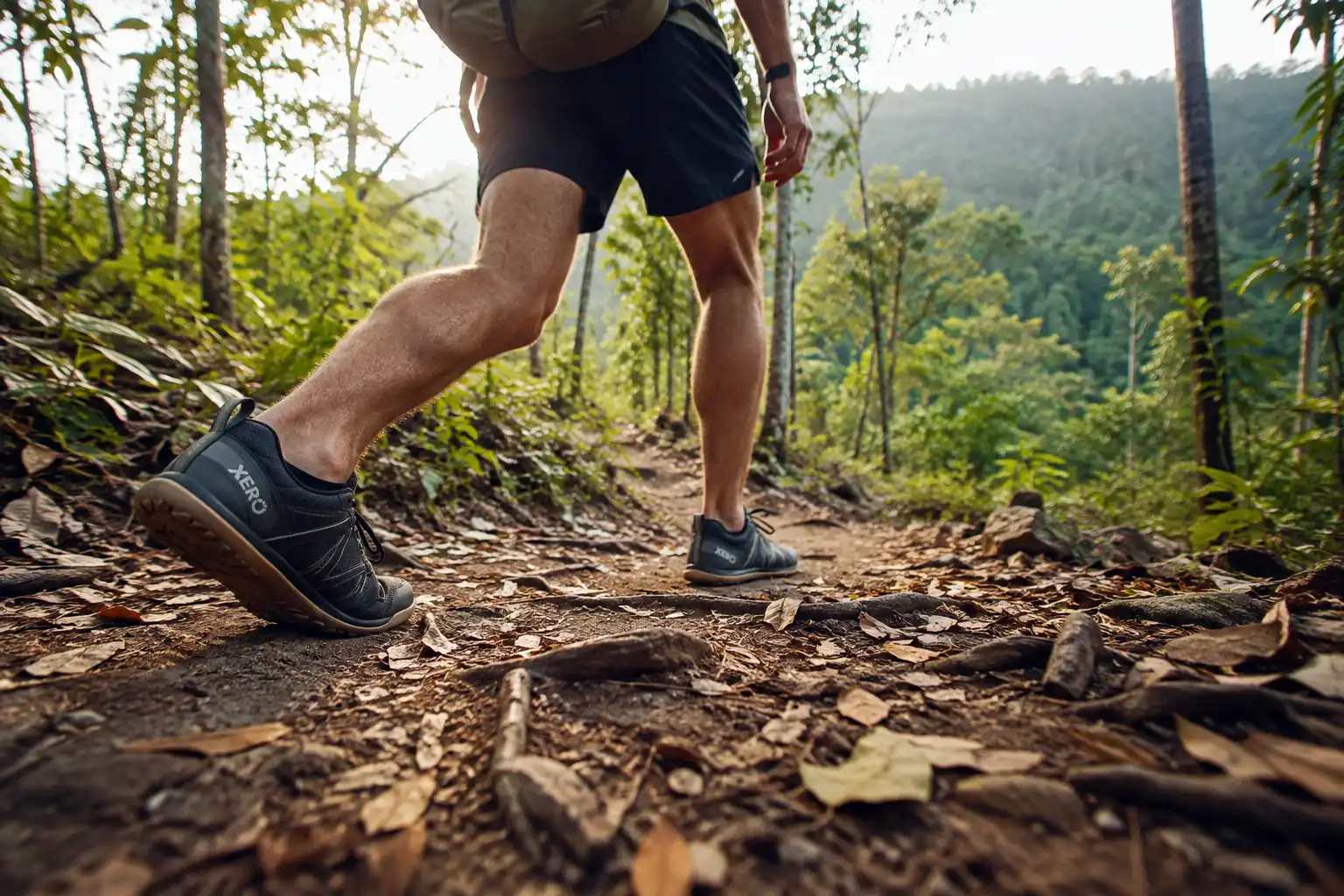 Hiker in minimalist barefoot shoes walking on a soft dirt trail through hill forest with a light daypack