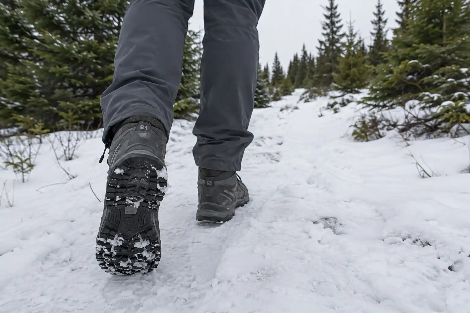 Hiker walking on a packed snow trail wearing mid-cut waterproof hiking boots in shallow snow