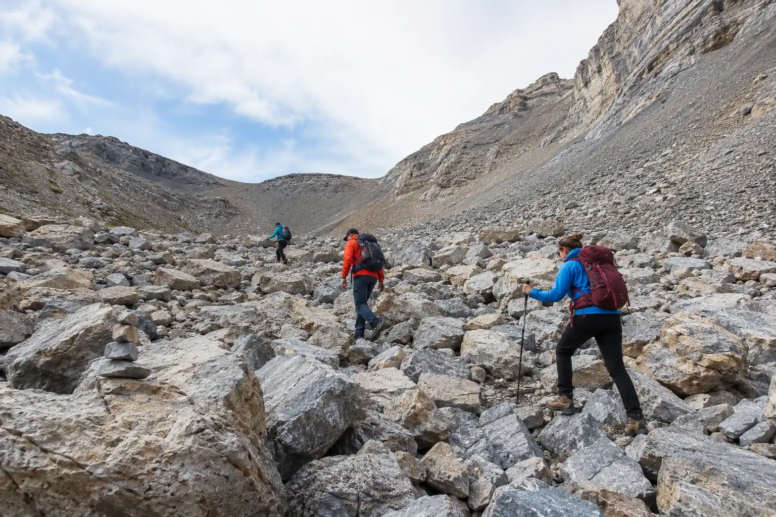 Hikers picking their way across a wide field of gray limestone boulders on the Mount Timpanogos trail with trekking poles for balance