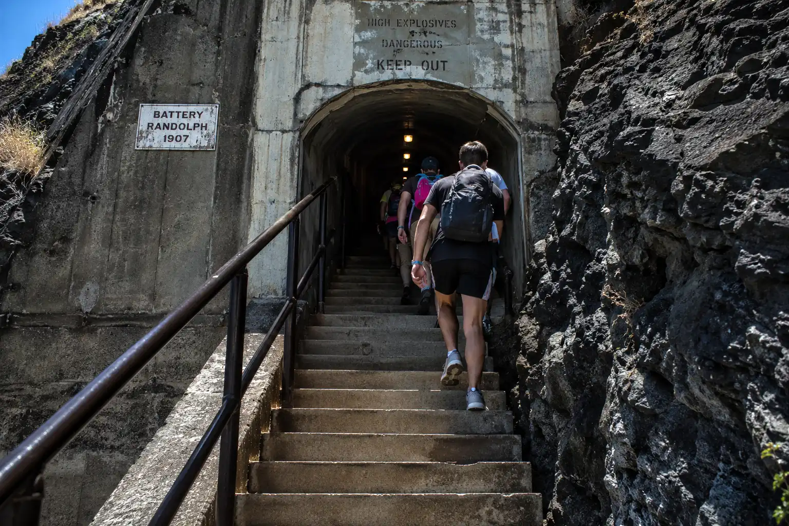 Hikers climbing steep concrete stairs toward a lighted tunnel entrance near the top of the Diamond Head trail