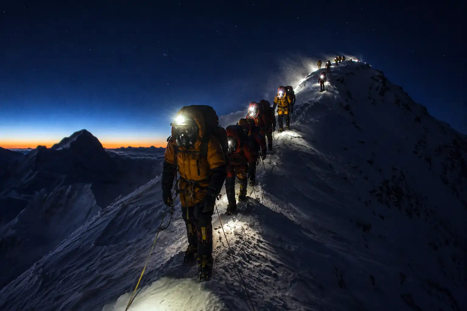Row of climbers with headlamps moving up the snowy Southeast Ridge of Everest during a pre dawn summit push