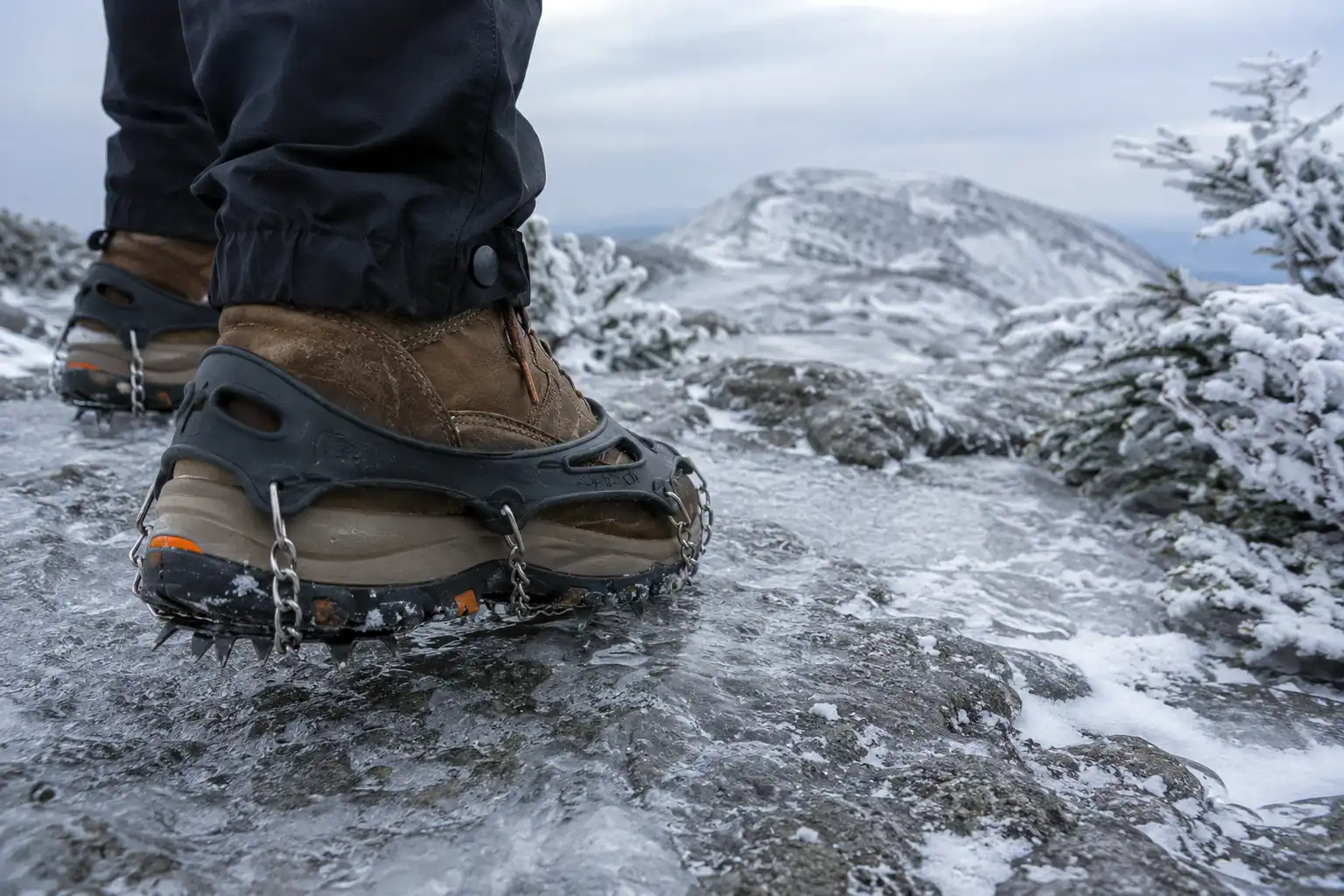 Close-up of microspikes fitted over hiking boots gripping an icy granite ledge on Mount Monadnock in winter