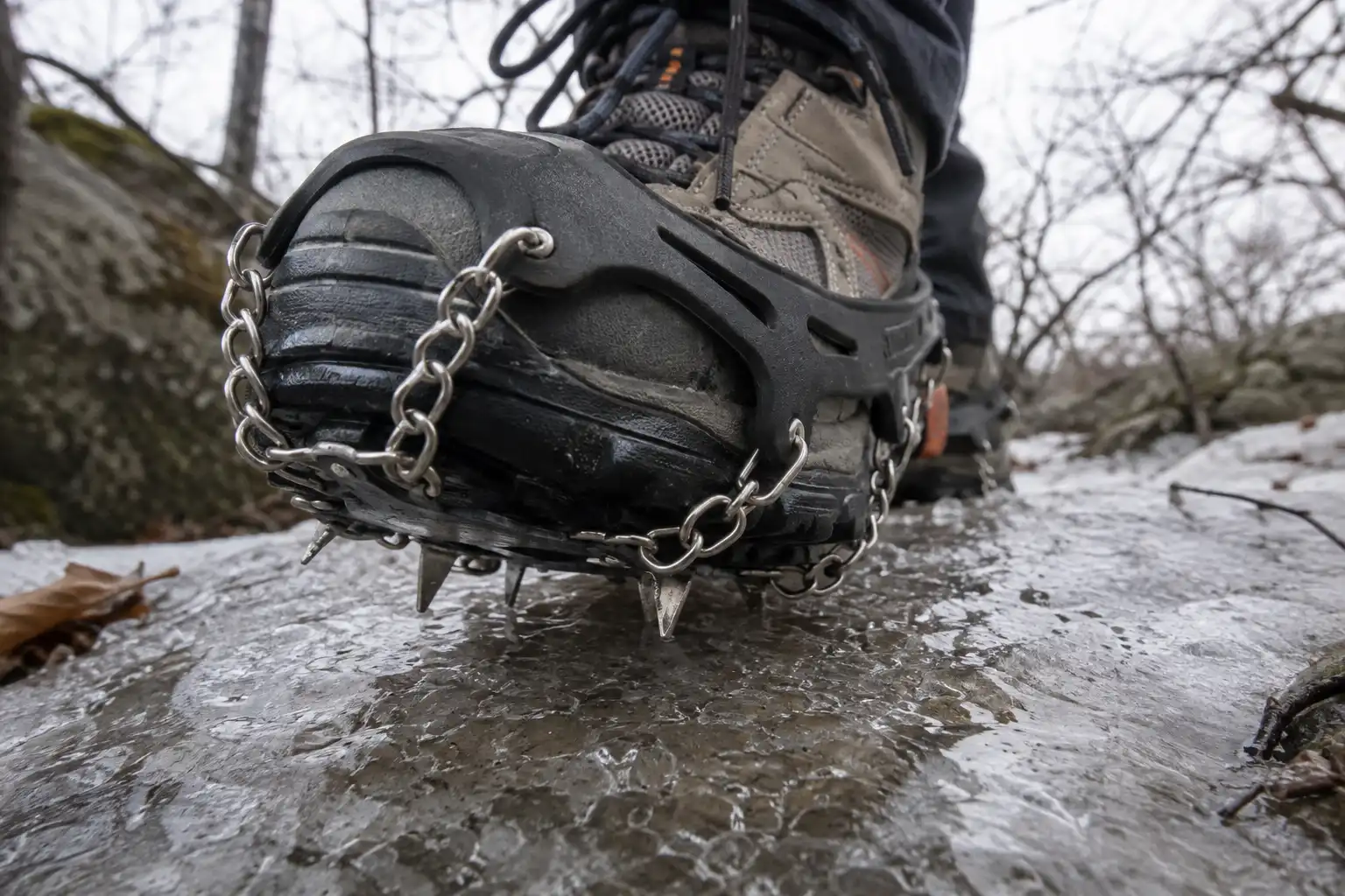 Microspikes with chains and steel spikes strapped over a flexible hiking boot standing on an icy packed trail