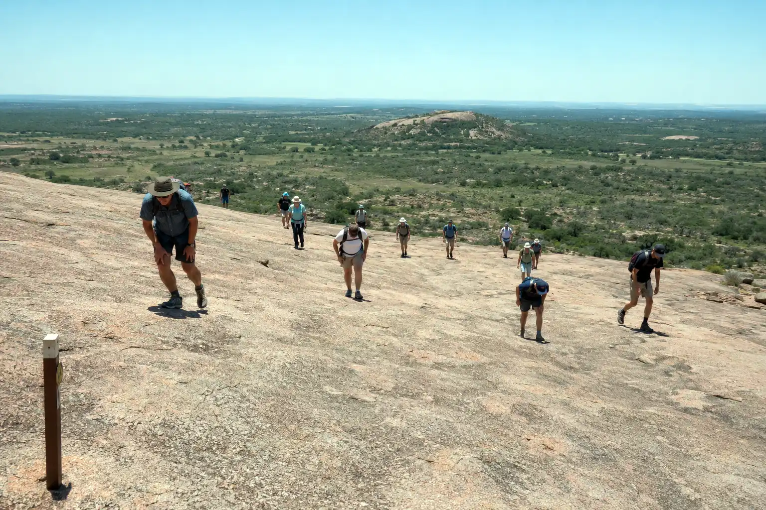 Hikers spread across the open granite slope of Enchanted Rock where the marked trail ends and people pick their own line to the top