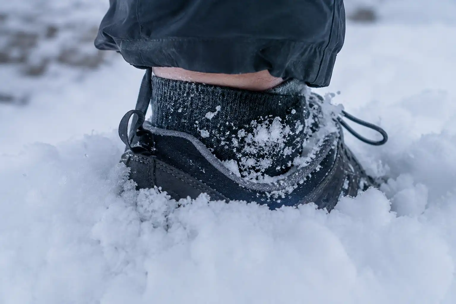 Loose snow falling over the ankle opening of a low cut hiking shoe as the wearer steps into a deeper drift