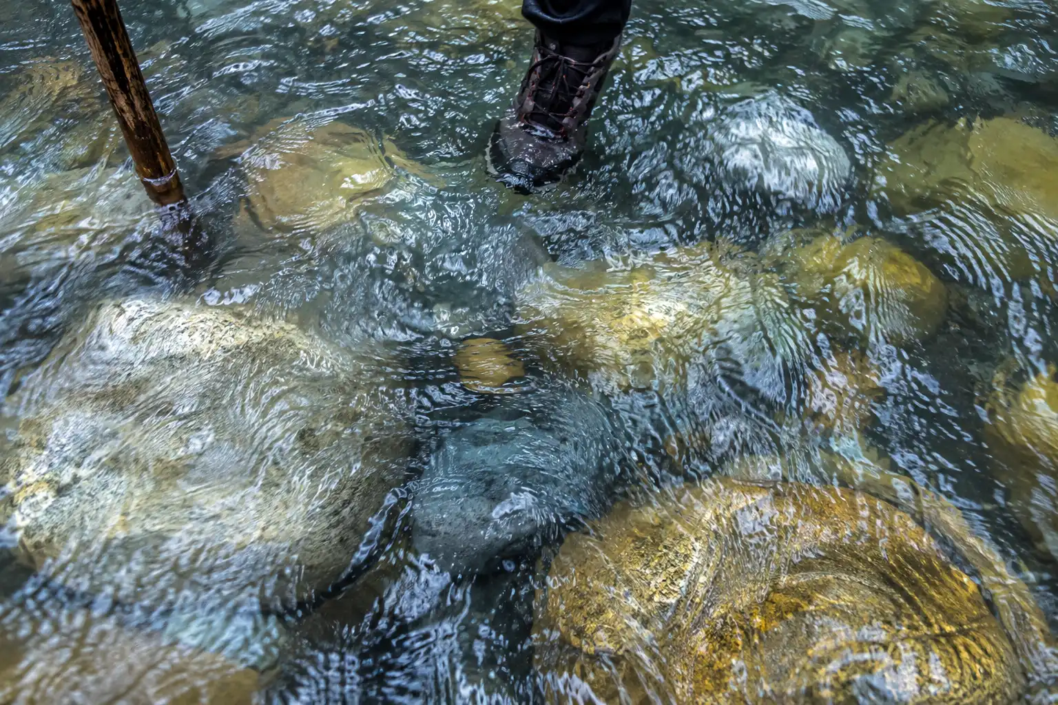 Close view of large rounded slippery boulders under fast-moving shallow river water showing why footing in The Narrows is unstable