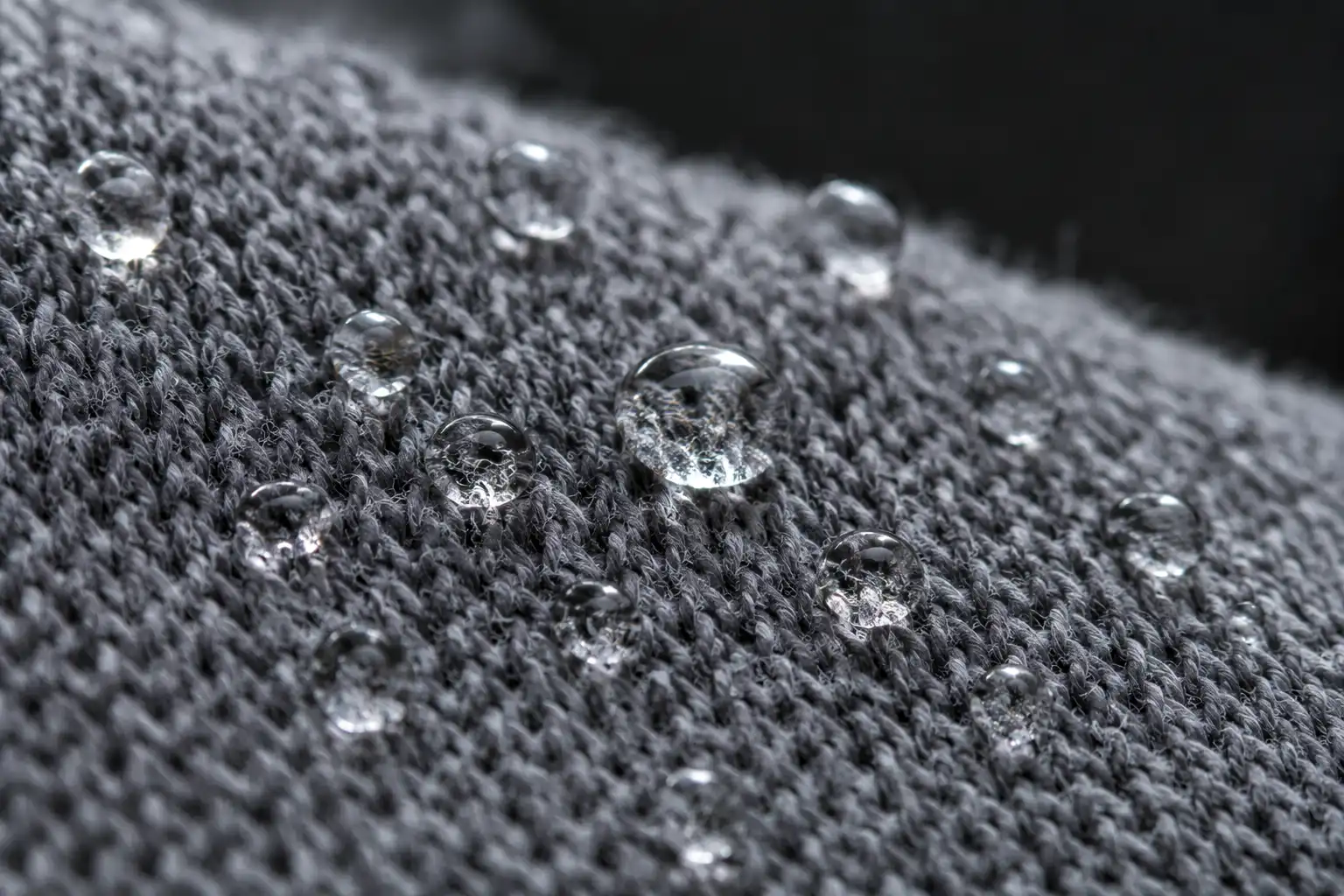 Extreme close up of water droplets sitting on the surface of a knit polyester hiking shirt without soaking in