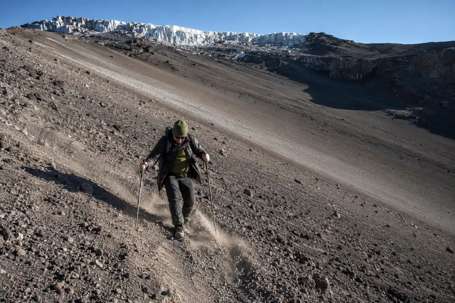 Trekker using trekking poles to descend a steep slope of loose volcanic scree on Kilimanjaro after summiting
