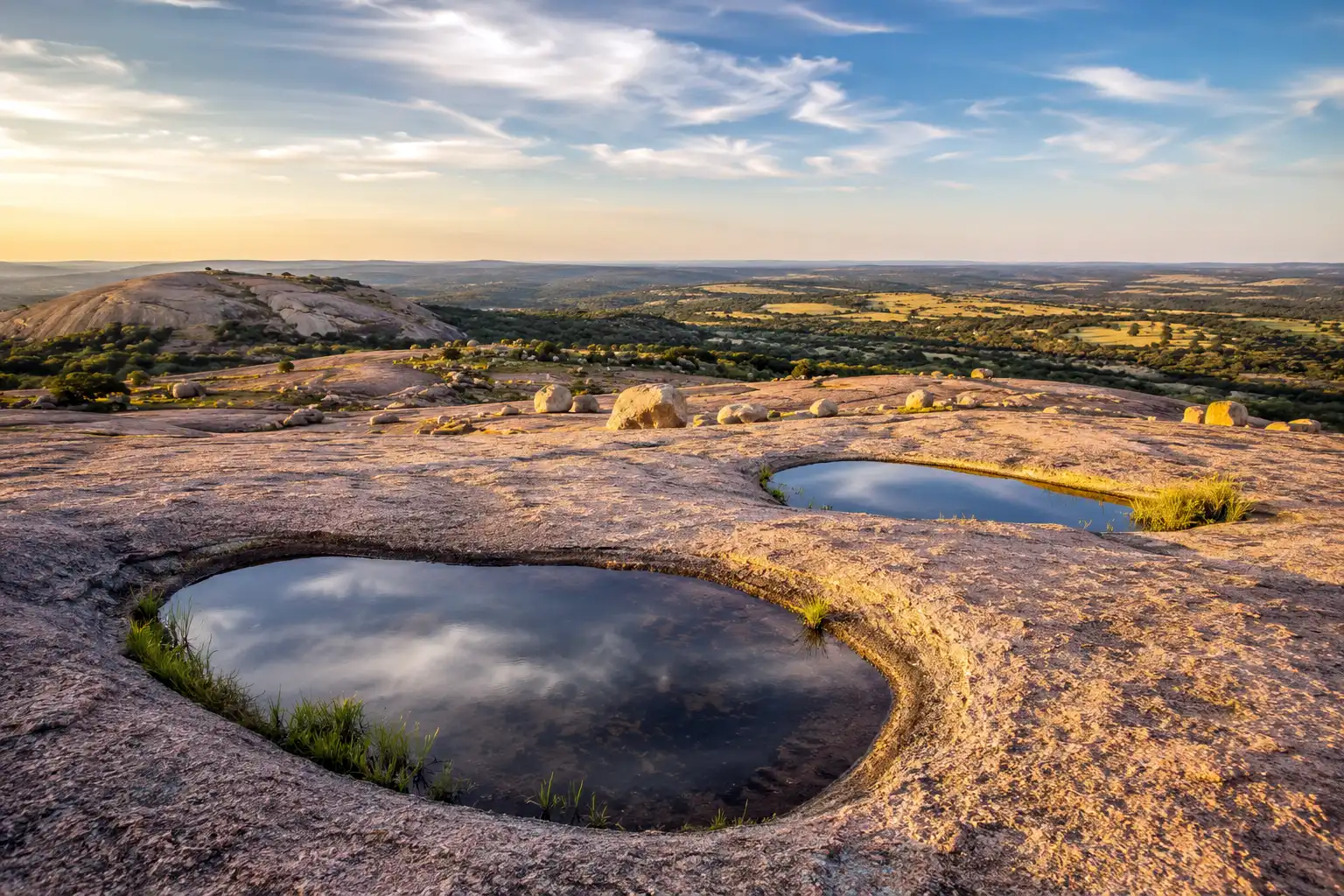Shallow rainwater vernal pools on the flat summit of Enchanted Rock with the Texas Hill Country stretching out behind