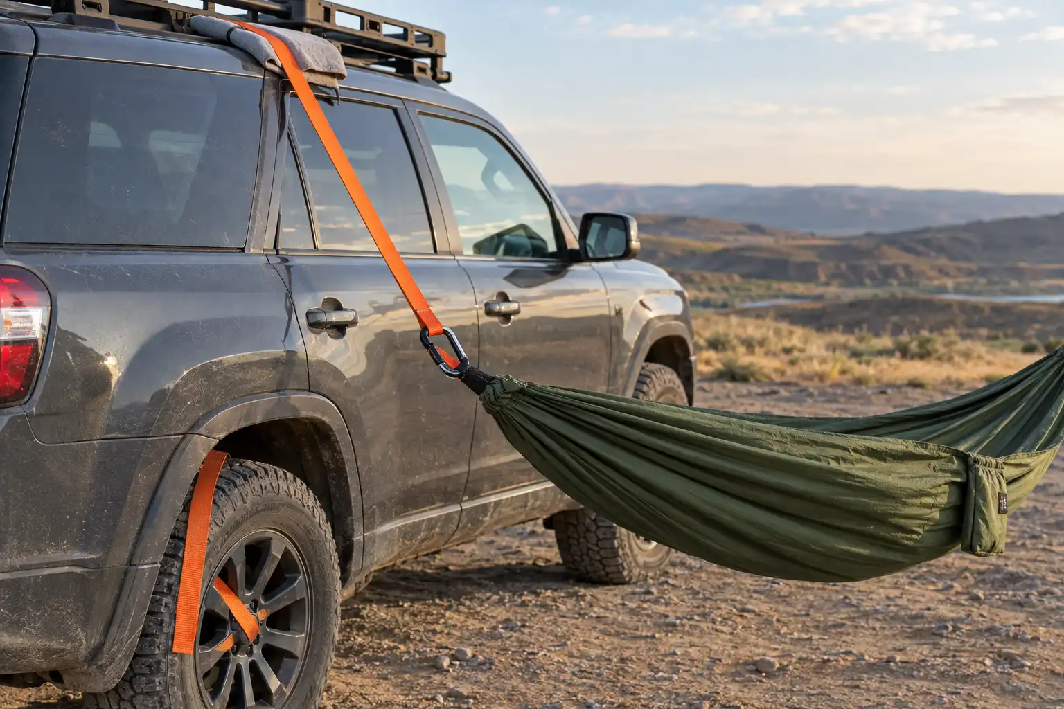 Webbing strap passing over the roof of an SUV and wrapped through the spokes of the far side wheel, with a hammock clipped to the strap on the near side