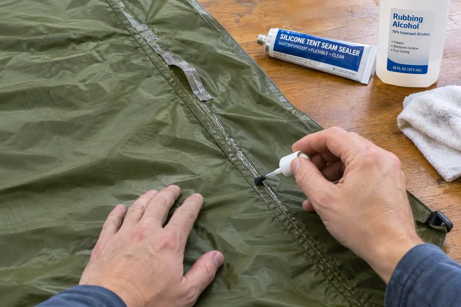 Person applying a thin line of seam sealer along the stitching of a rainfly laid flat on a table with a brush applicator