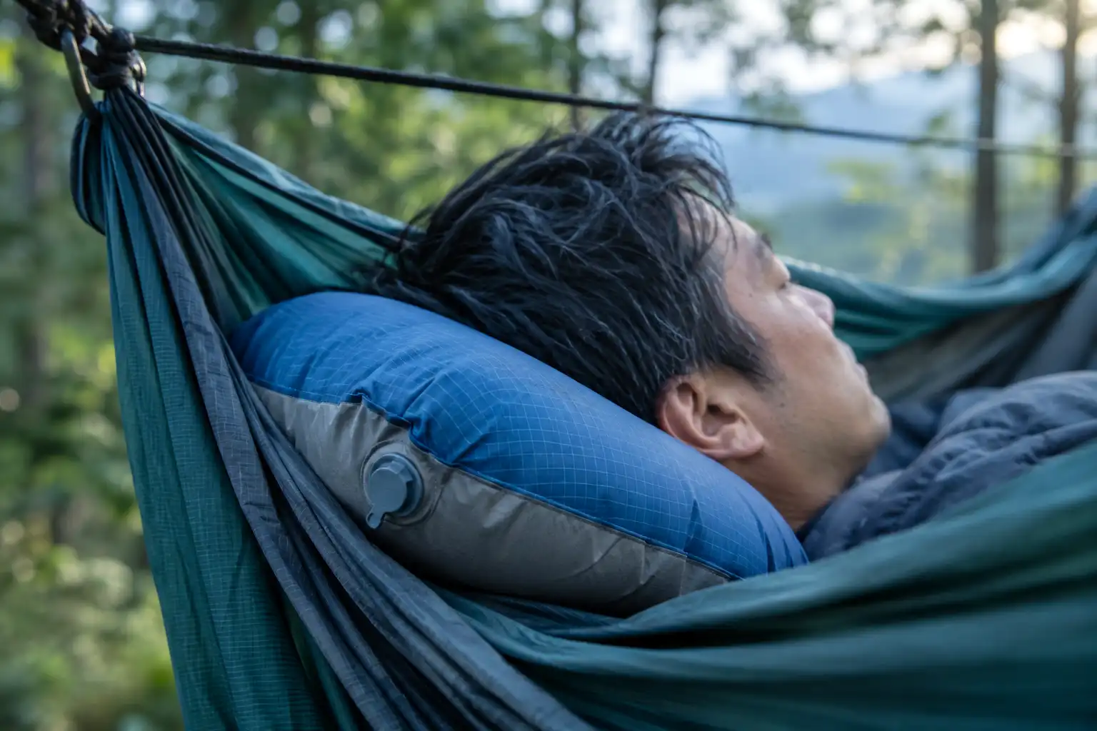 A small inflatable camping pillow supporting a sleeper's neck at the head end of a gathered end hammock