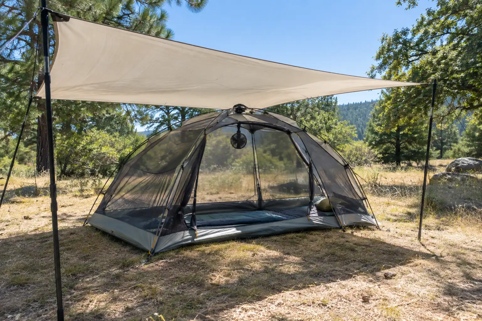 Tent with its rainfly rolled back to expose mesh panels, shaded by a separate tarp strung on poles above it at a sunny campsite